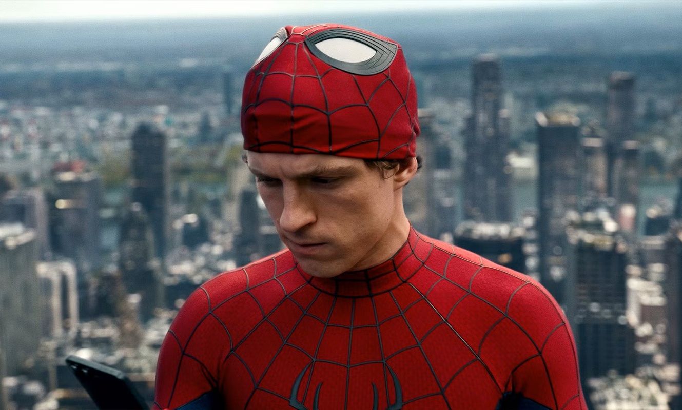 Spider-Man in a red web-pattern suit stands on a city rooftop, looking down at a phone against a blurred skyline.